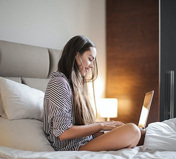 A woman sitting on a bed while using a laptop