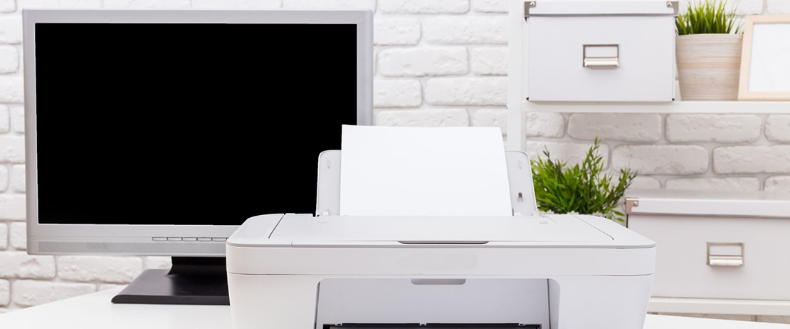 A white printer next to a computer in front of a white brick wall