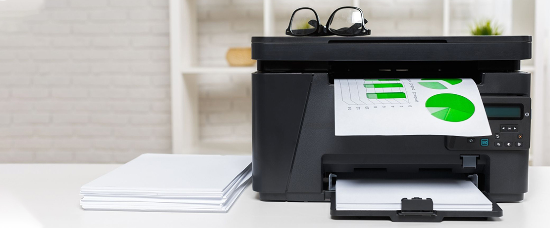 A pair of glasses on top of a black printer that is printing documents
