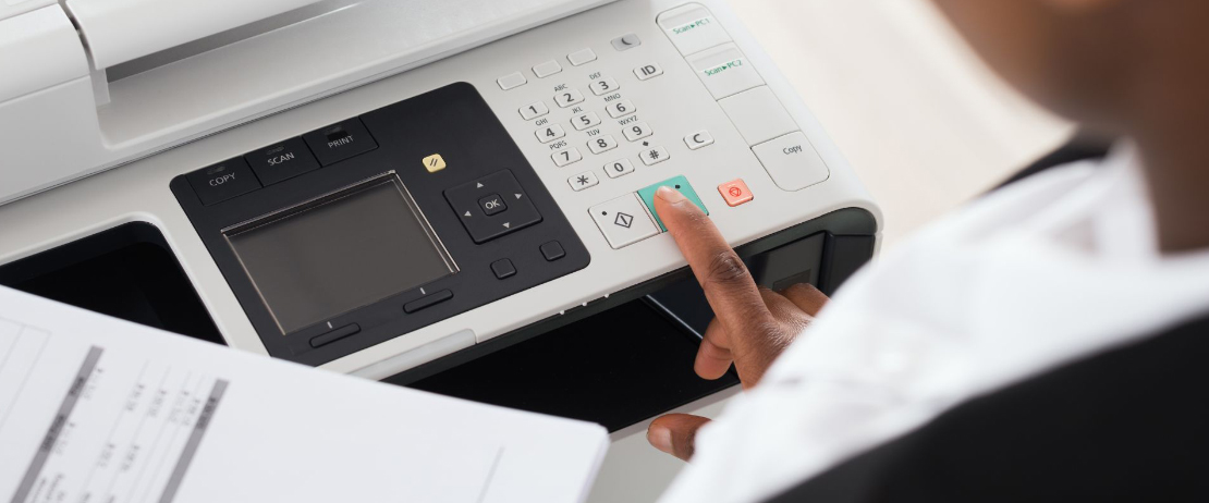  An employee presses the power button of a multi-function printer to begin printing