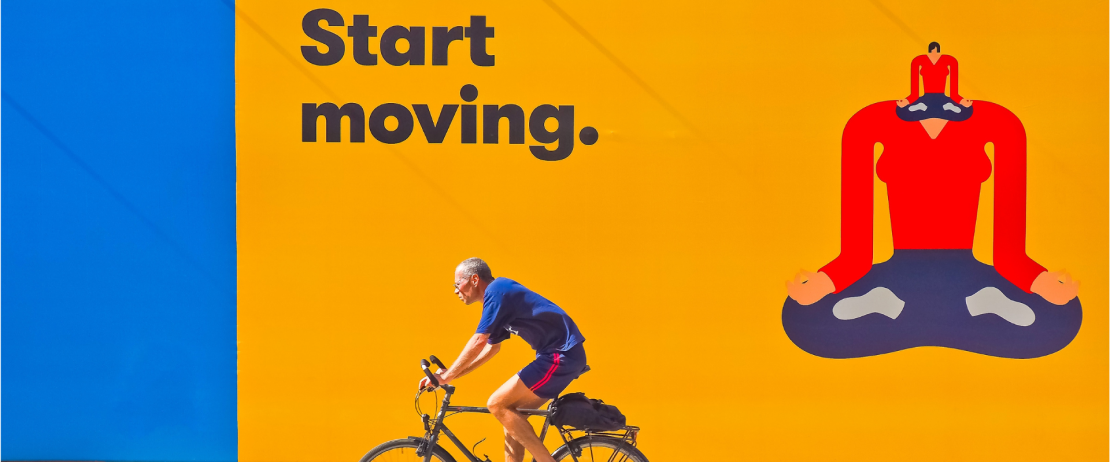 a man riding a bike past a large format print advertisement that says “Start moving.”