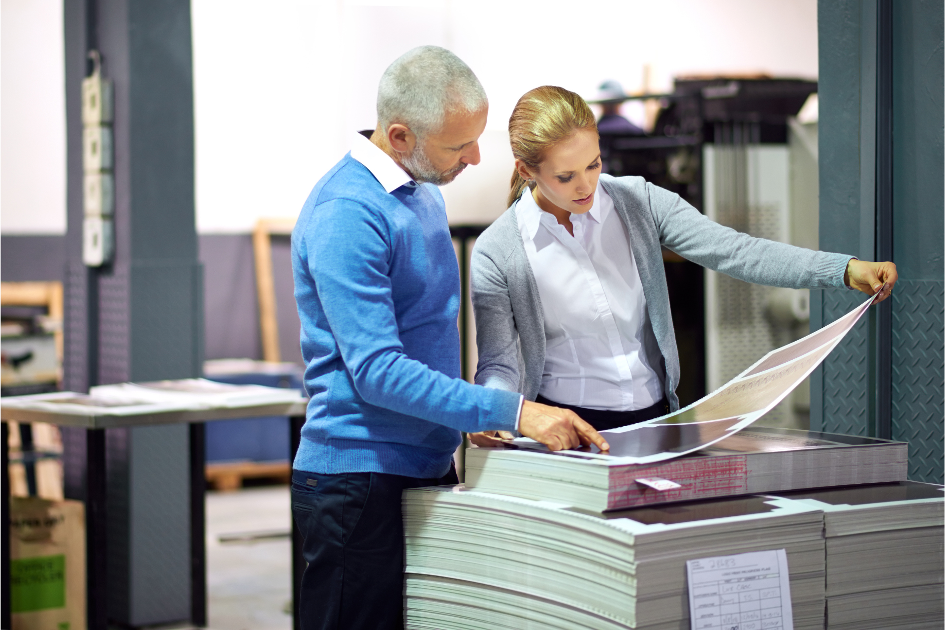 Two editors review printed packaging materials in a publishing warehouse