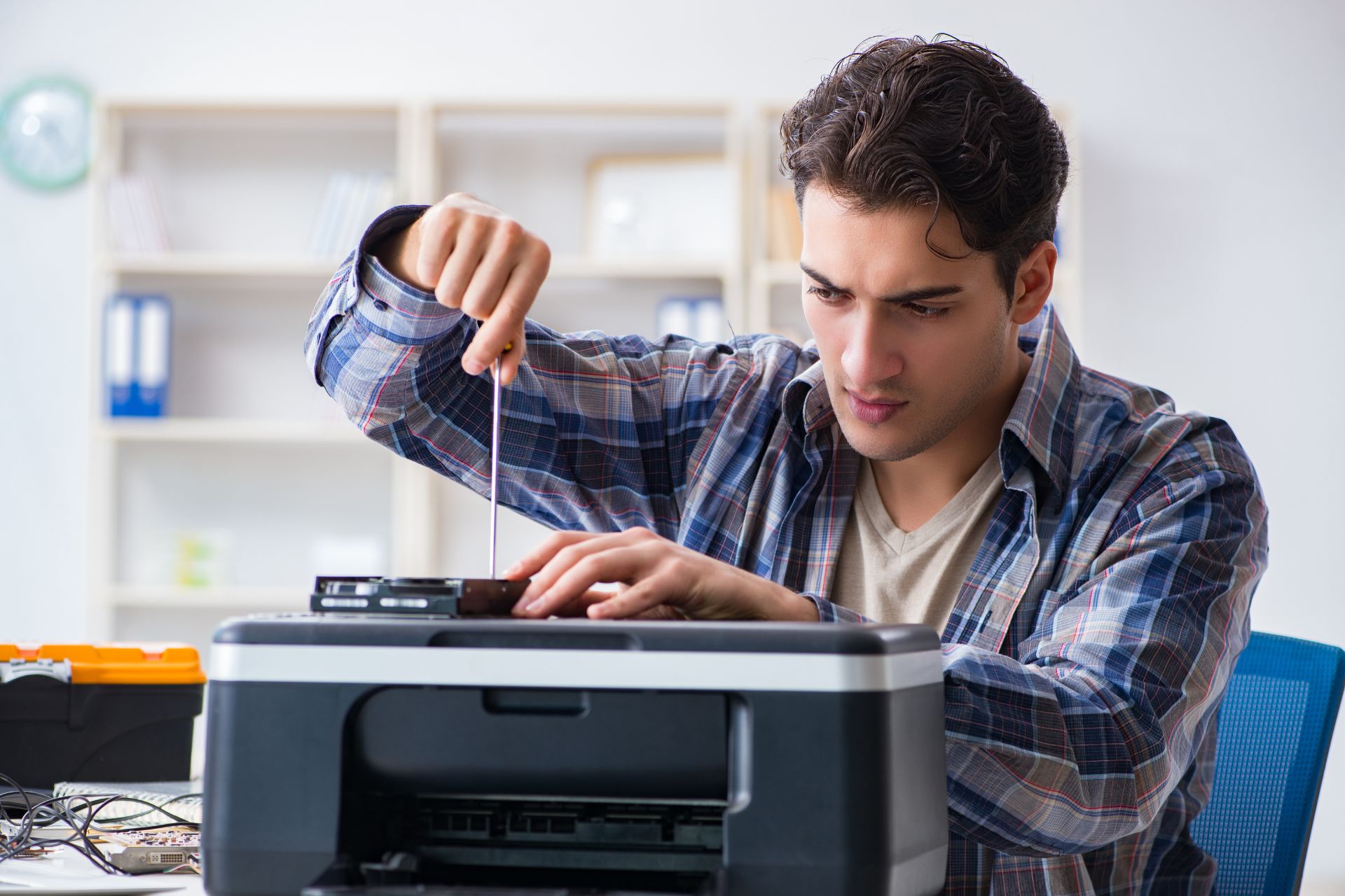 A man attempts to fix his home office printer with a screwdriver