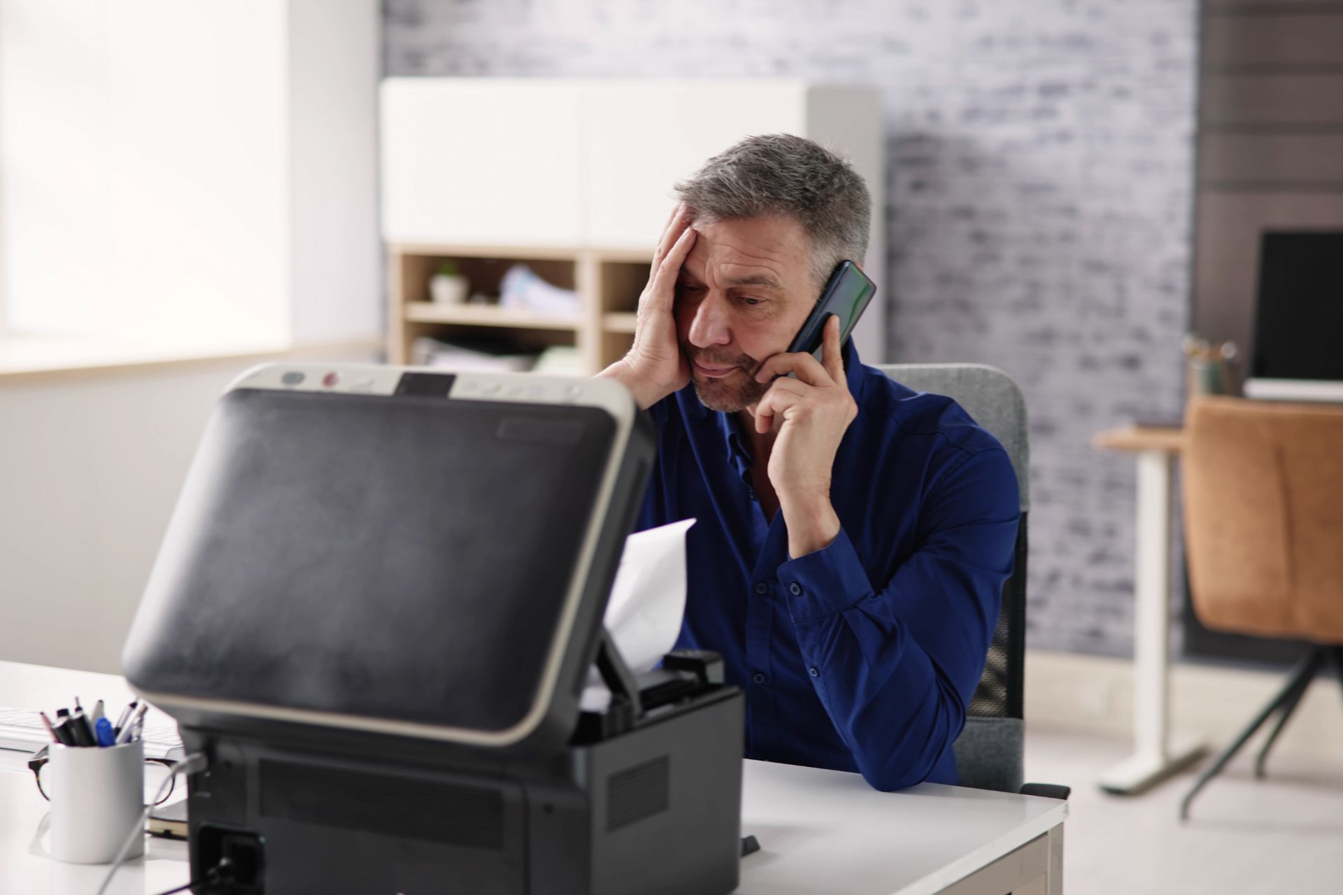 A frustrated man on the phone dealing with a broken printer