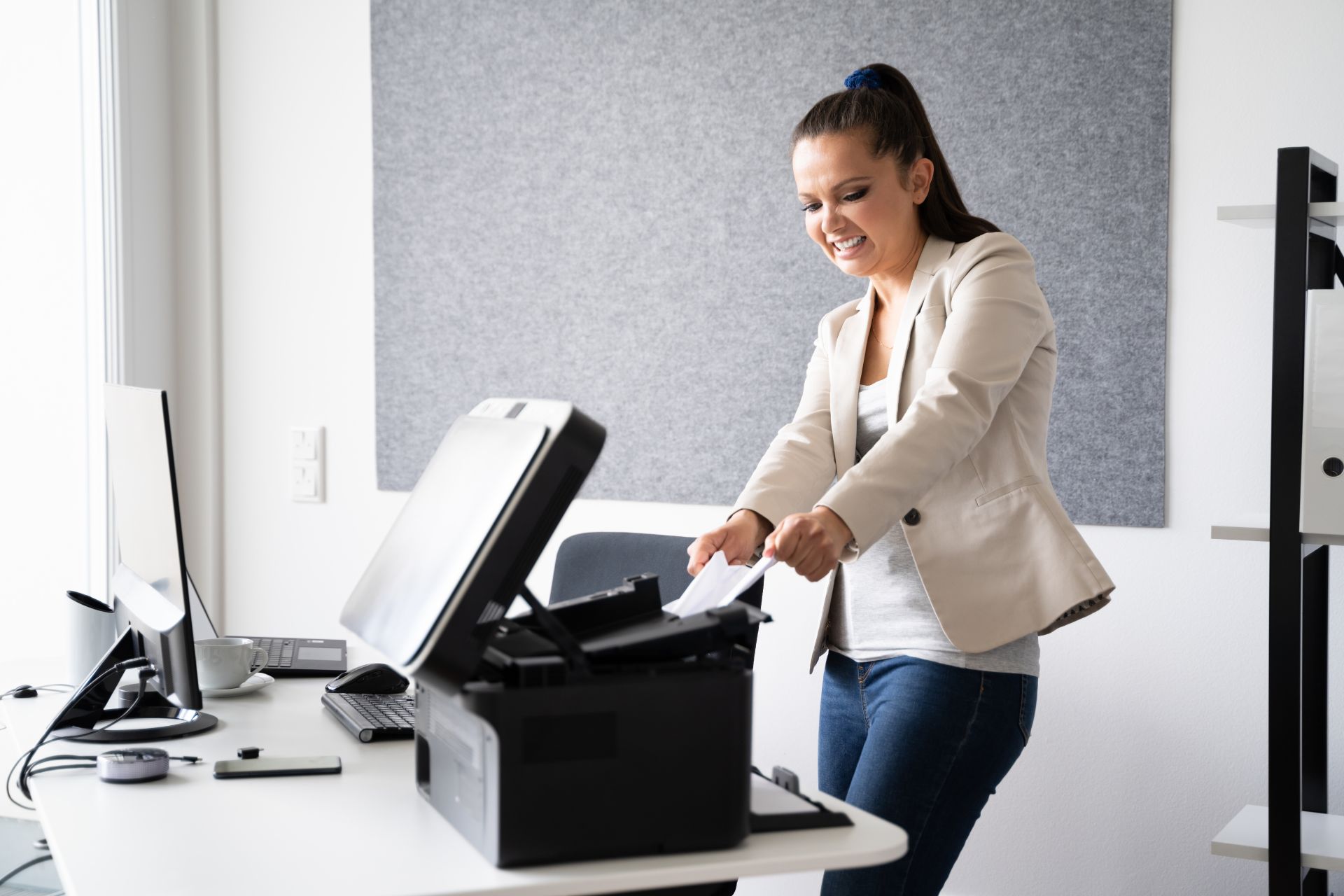 A frustrated woman pulls a piece of paper from a black printer