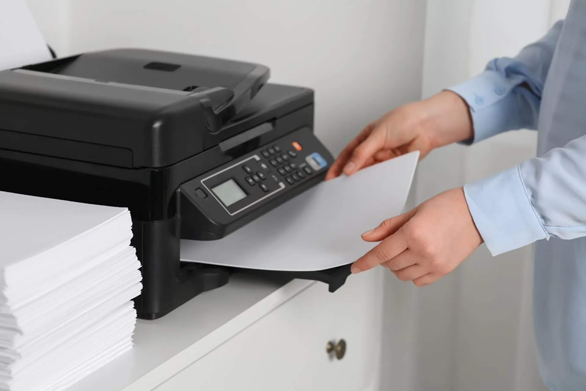 A woman at an office loads paper into a printer tray