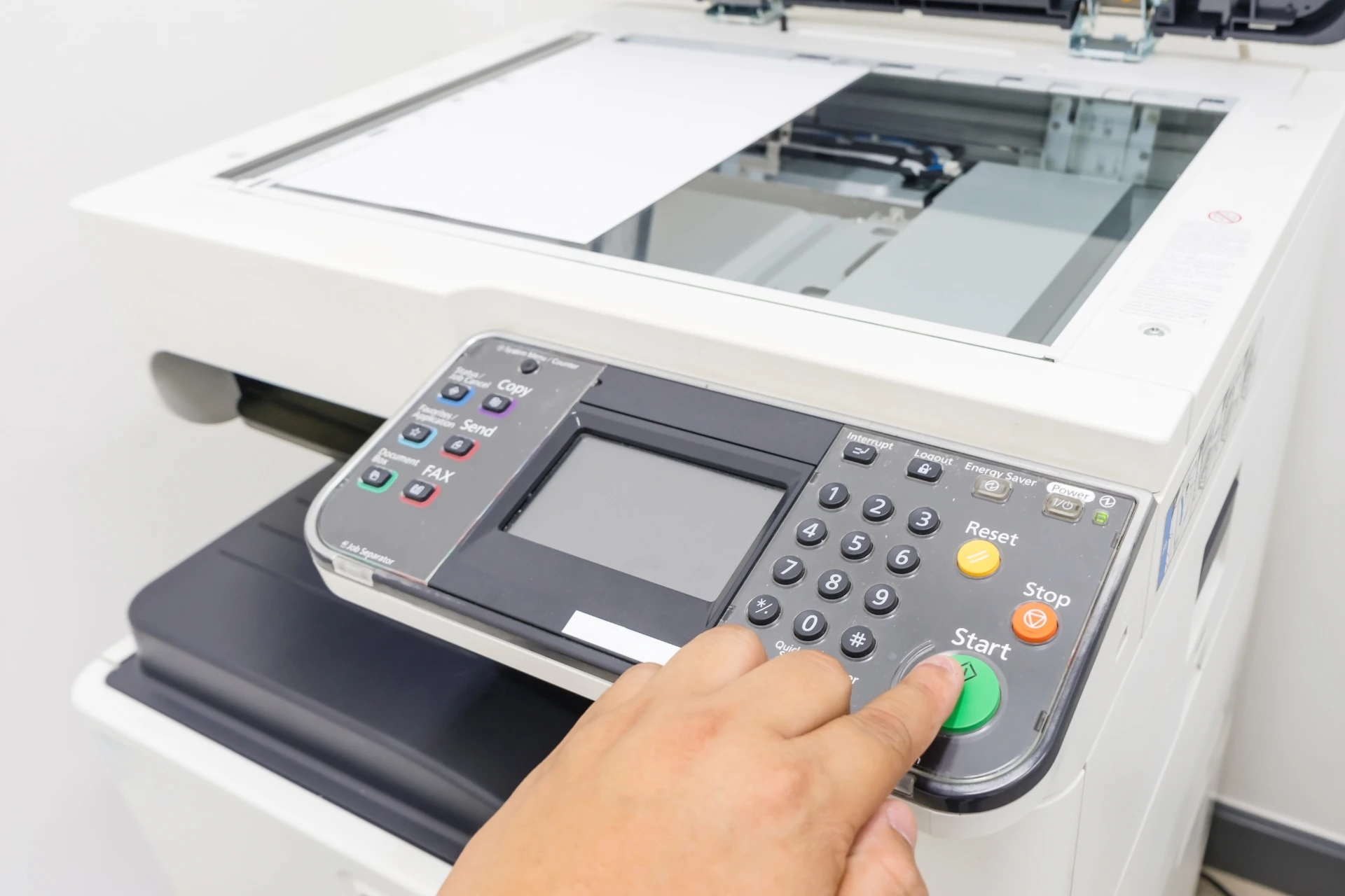 A finger pressing the start button on an MFP with a document on the flatbed scanner